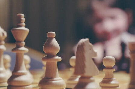 A close up shot of wooden chess pieces with a person out of focus in the background
