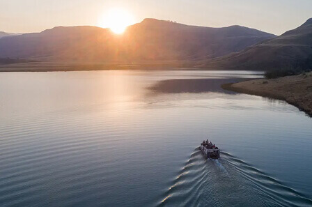 A boat on a large dam with the sun setting behind a mountain in the distance