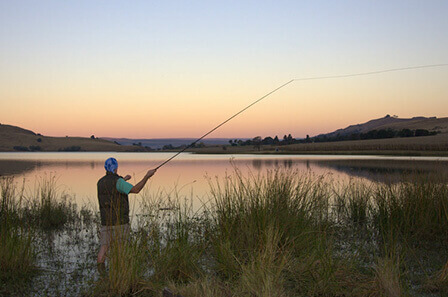 A man in the early morning casting his rod into a dam to catch fish