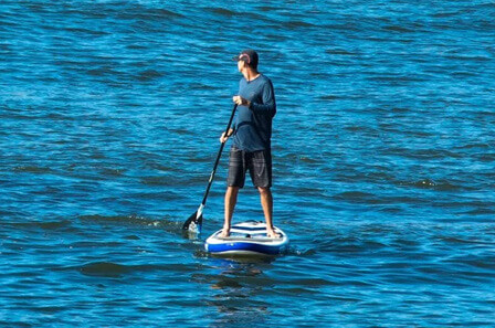 A man in open water standing on a paddle board looking behind himself