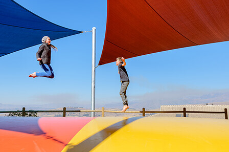 Two people jumping up and down on a large and bright jumping pillow