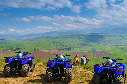 Three quad bikes are parked in a row whilst two people sit and take in the view