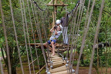 A young child navigates a challenging rope bridge in the Rope Adventure Park