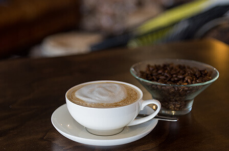 A close up view of a hot beverage and a small glass bowl containing coffee beans