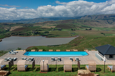 An ariel view of a large swimming pool and deck area overlooking the dam and mountains